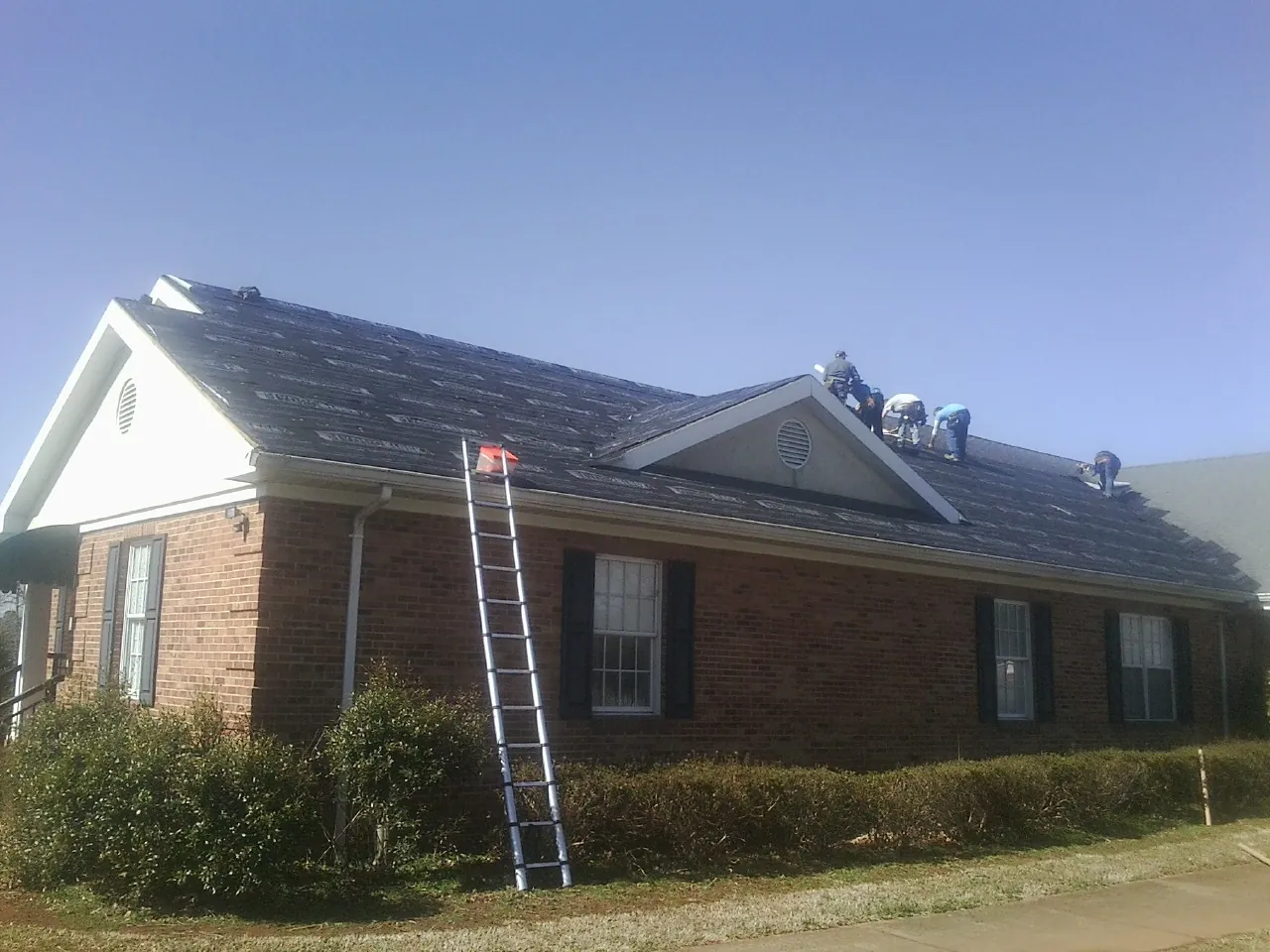 Crew tearing shingles off a brick ranch roof with a ladder set — Metal Roof Repair work by our crew in Lanesborough