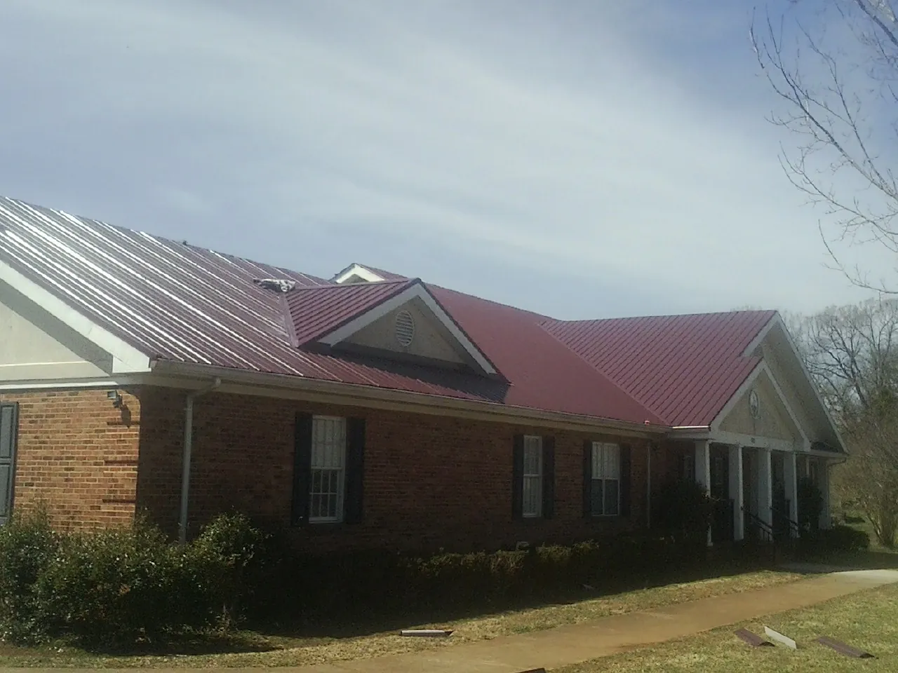 Red metal roof with gabled entries on a long brick building, from a Hail Damage Roof Repair job in Lanesborough