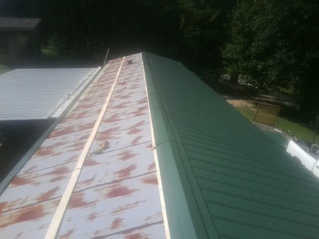 Old rusted panels beside newly installed green metal roofing — Wind Damage Roof Repair by Roofing Brothers in Lanesborough