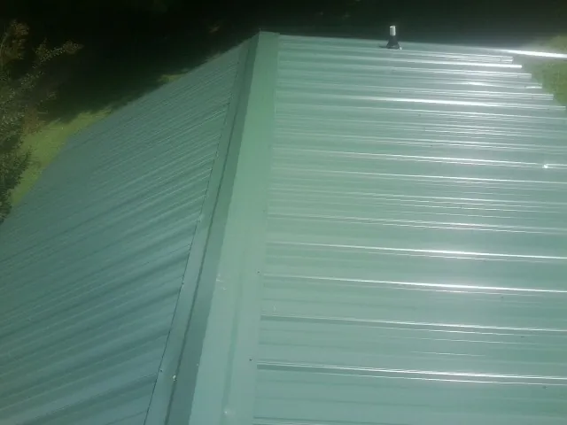 New green metal panels meeting at the ridge of a roof — Flat Roof Repair work by our crew in Lanesborough