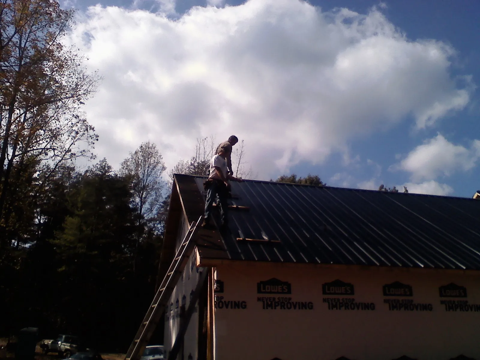 Roofer fastening dark metal panels high against a cloudy sky, from a Roof Inspection job in Lanesborough