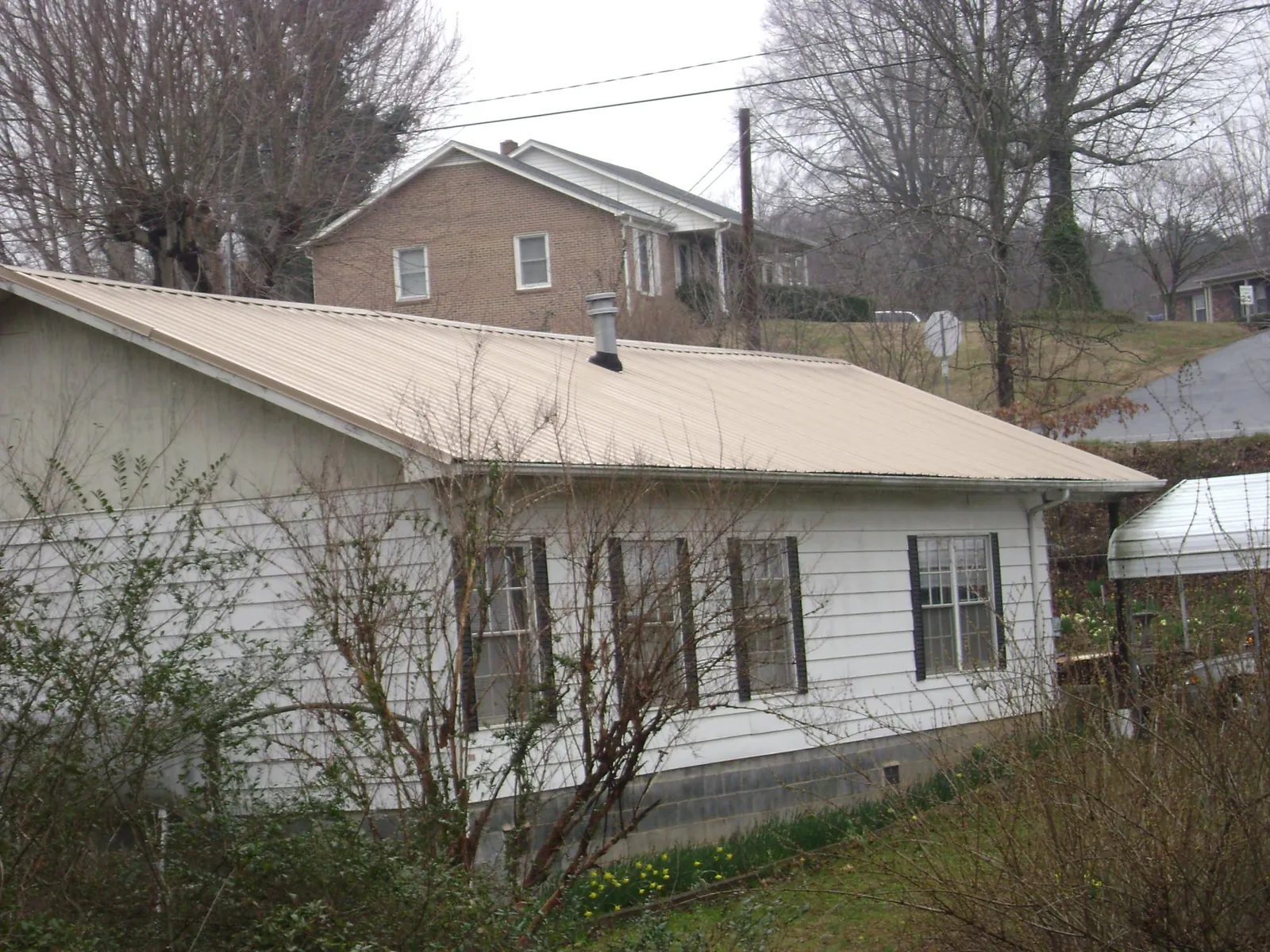 Tan metal roof on a white sided house set into a hillside — Commercial Roofing by Roofing Brothers in Lanesborough